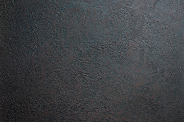 Close-up detail of dark textured stucco wall surface showing rough aggregate finish and weathering patterns
