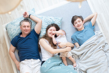 Obraz premium father and three children lying in bed, having fun in the morning, top view