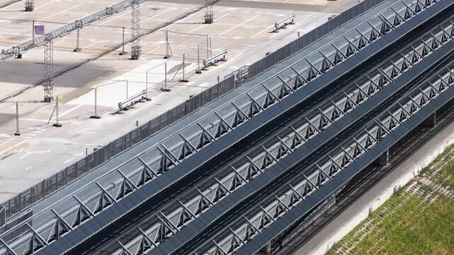 Elevated view of a modern multi-tier parking facility with metal ramps and a riverside promenade featuring cyclists and urban greenery.