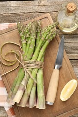 Fresh raw asparagus spears, knife, lemon and oil on wooden table, flat lay