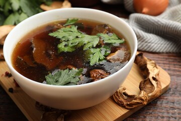 Tasty soup with mushrooms and parsley in bowl on wooden table, closeup