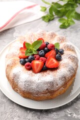 Tasty Bundt cake with powdered sugar and berries on grey textured table, closeup