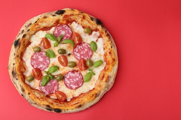 Delicious pizza with salami, olives, tomatoes and basil on red table, top view. Space for text