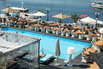 Beautiful swimming pool, sunbeds, tables, chairs and umbrellas near sea on sunny day
