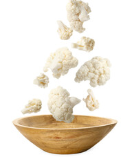 Cauliflower florets falling into bowl against white background
