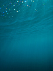 Light filtering down through blue water. Underwater sunlight in deep sea. Sunlight viewed from blue abyss, slow motion. Underwater sunlight shining deep under water with ripples on wave surface. sun.