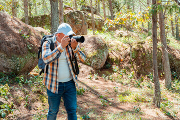 Photographer taking a picture in forest with camera and backpack