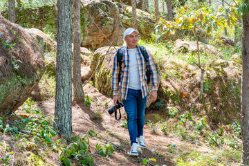 Happy photographer walking through a sunny pine forest with camera in hand