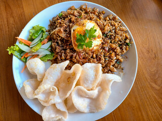 A delicious plate of Indonesian Nasi Goreng (fried rice), served with a fried egg, crispy prawn crackers, and fresh pickles. A famous and popular dish from Indonesia.