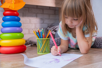Child drows on the floor with colorful pencils in cozy living room