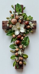 Rustic wooden cross adorned with lush green leaves, delicate white blossoms, and brown seed pods, arranged artfully