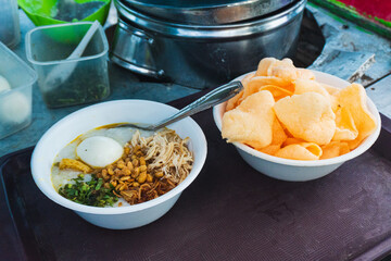 Chicken porridge. A mixture of rice, boiled egg, soybeans, shredded chicken, cracker, and vegetables, typical Indonesian food served as breakfast.