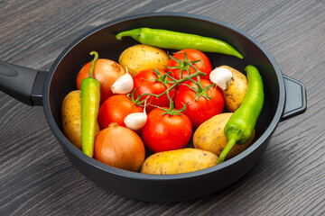 Fresh vegetables in a black pan with garlic and green peppers on a wooden table