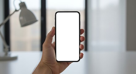 Hand holding smartphone with blank screen, modern interior background.