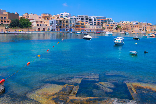 BIRZEBBUGA, MALTA - May 25, 2023: the Colorful small fishing boats moored with buoys in St George's Bay, in Birzebbuga, Malta