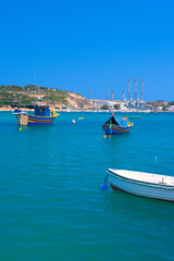 Fototapeta premium BIRZEBBUGA, MALTA - JUNE 28, 2023: the Colorful small fishing boats moored with buoys in St George's Bay, in Birzebbuga, Malta. This was on a sunny afternoon.