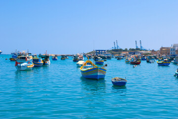 Obraz premium BIRZEBBUGA, MALTA - May 25, 2023: the Colorful small fishing boats moored with buoys in St George's Bay, in Birzebbuga, Malta