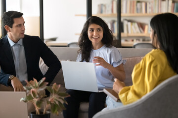 Indian woman conduct meeting with staff members sit on sofa with laptop, presenting new ideas for start-up, discussing joint task or online project, developing marketing strategy at briefing in office