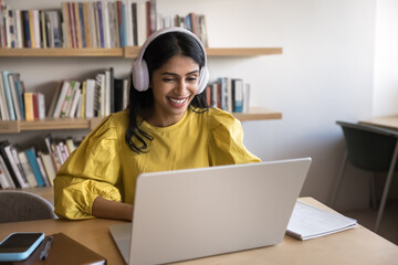 Indian woman wear headphones participate in video call by business or study using laptop and...