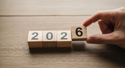 Hand placing wooden block with '6' to form '2026'
