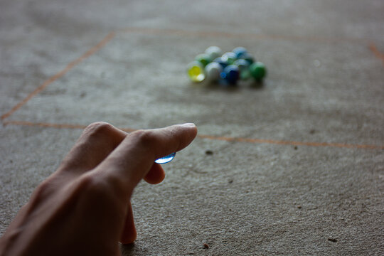 A person playing a game of marbles, aiming to shoot at a group of marbles in a square. Concept of childhood games, nostalgia, and recreation.