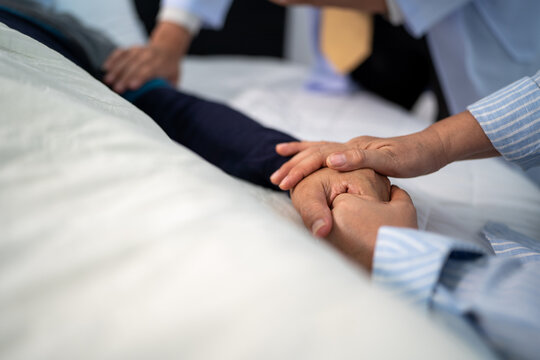 scene of bedridden patient, focus on hand of wife holding hands illness elderly hopeless senior man. home caregiver nurse visit retirement patient for health check up recovery process medical service