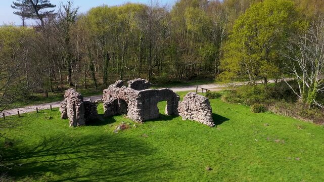 Over ruins of the Roman Bath House to Ravenglass village on mouth of River Esk on W coast of Cumbria, England. Site of Roman port of Itunocelum sits in woodland. 4k video fly up out