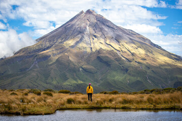 Woman stands by Pouakai Tarn, admiring the mighty Mount Taranaki, Egmont National Park, North Island, New Zealand