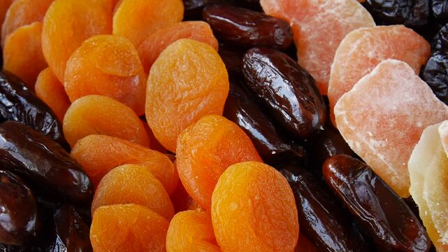 Close up of dried apricots, dates, crystallized ginger and prunes rotating on a wooden table.