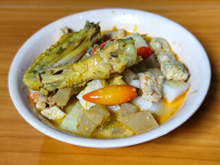 Traditional Indonesian vegetable lontong dish. Lontong opor ayam with sliced chayote, carrots, tofu and sliced red chilies, served in a white ceramic bowl on a wooden table.