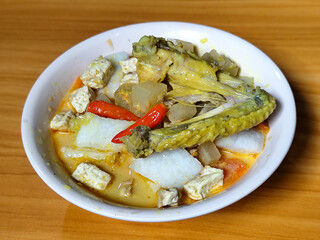Traditional Indonesian vegetable lontong dish. Lontong opor ayam with sliced chayote, carrots, tofu and sliced red chilies, served in a white ceramic bowl on a wooden table.