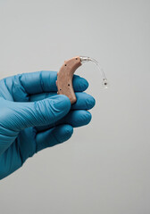 A hand in a blue glove holds a hearing aid against a plain background, emphasizing its design and technology.
