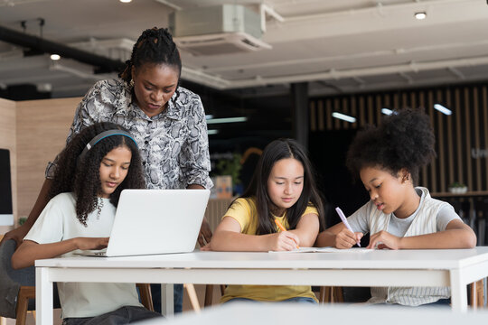 Female teacher teaching student using laptop computer in classroom. Student e-learning on laptop computer. Teacher assistance student using computer class in classroom - Powered by Adobe