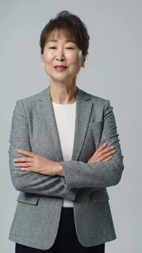 A confident diverse professional in smart-casual business attire maintains eye contact with a subtle smile, uncrossing arms to an open gesture. Video transitions from MCU to MS against a minimalist