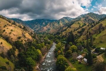 High-angle view of a river winding through a valley nestled between rugged mountains.  Rolling hills, lush green foliage, and a flowing river are visible.  Cloudy sky above