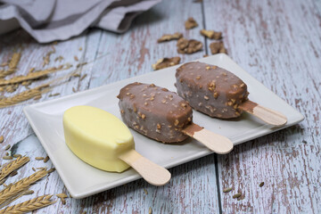 Delicious scene with three ice cream bars, including chocolate and vanilla flavors, served on a white plate with toppings, seeds, nuts, and colorful sprinkles. 