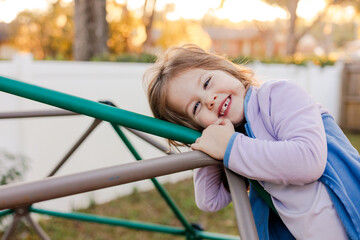 Fototapeta premium Smiling Young Girl with Missing Tooth Leaning on Jungle Gym