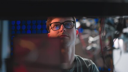 Close-up of focused person in glasses working at a computer, concentrating on tasks in a studio environment, illuminated by bright background lights, with reflections in glasses