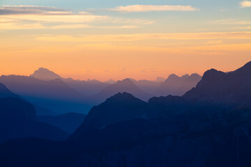 Distant mountain peaks layers at sunrise. Pattern of mountains silhouettes against orange sky in Dolomites.