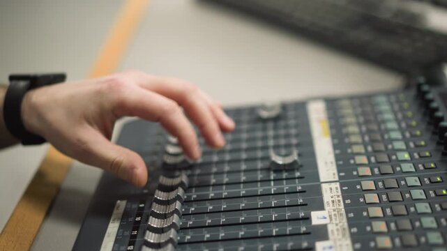 Close-up of hand adjusting fader on audio mixing console, controlling sound levels, professional broadcast studio or control room, focused on precise sound control and engineering