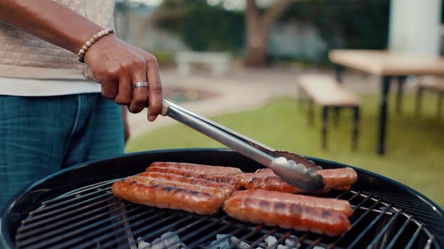 Hand, barbecue and grill sausage for party or new year celebration in backyard with food. BBQ, cooking meat and person with tongs outdoor for lunch preparation, meal and cookout event on weekend