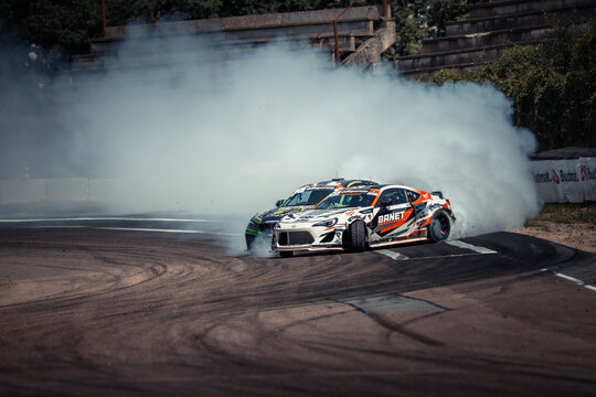 Two race cars are speeding around on a dirt track, creating a lot of smoke as they drive
