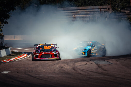 Amidst the fiery chaos of a high-speed race, two racing cars vie for dominance on the track, their engines roaring and smoke billowing into the air