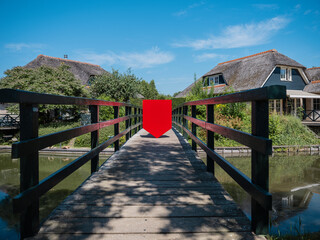 Physical red shield on wooden bridge with village backdrop for scenic branding applications