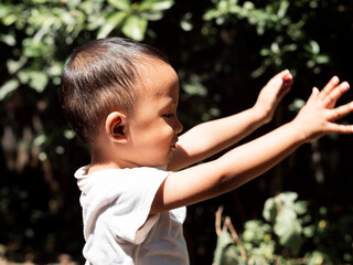 Side portrait of a handsome child, adorable boy in white t-shirt looking through his shoulder at camera, with summer natur background. Copy ad space.