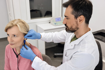 Audiologist meticulously fitting a hearing aid for a patient, using advanced equipment in a modern...