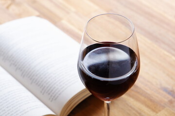 Glass of red wine with open book on table