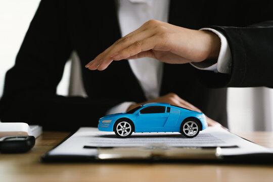 A person in a business suit gently shields a toy car, symbolizing automobile protection, vehicle insurance, safety, and responsible coverage in legal and financial services.