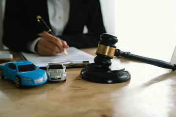 A lawyer uses a gavel near a toy car, symbolizing legal proceedings, car insurance claims, court decisions, accidents, liability, and justice in automotive-related legal cases.