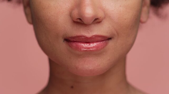 Close-up of smiling lips with lip gloss on pink background